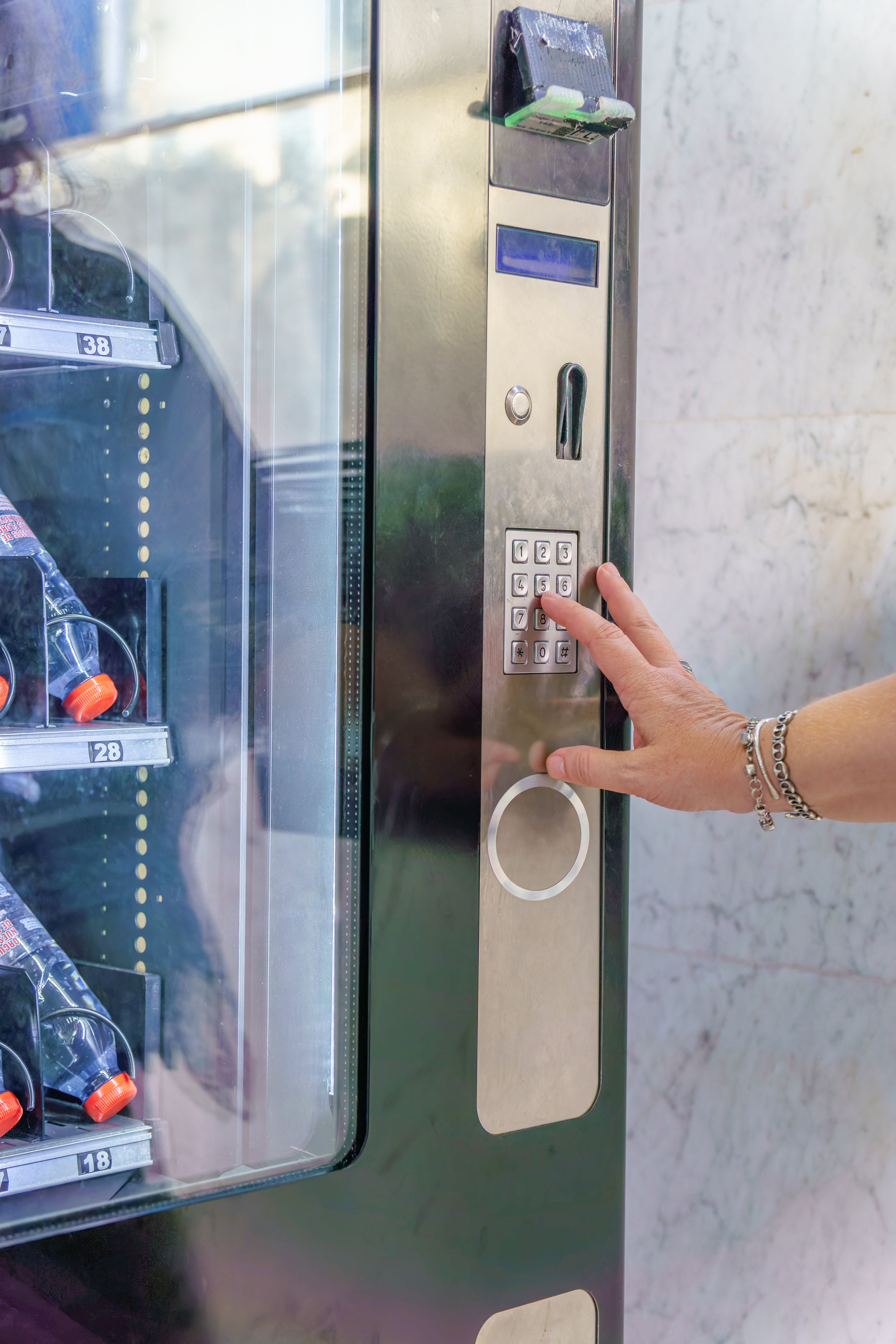 Hand inserting code on keypad of vending machine selling beverages